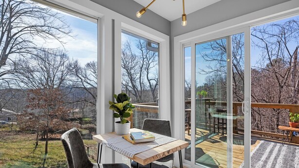 A modern room with large windows, a wooden table, two chairs, and a potted plant. - Bright and Tranquil Guesthouse! (Woodfin)