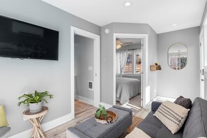 Ein modernes Wohnzimmer mit einem grauen Sofa, einem kleinen Beistelltisch mit einer Pflanze und einem an der Wand befestigten Flachbildfernseher.