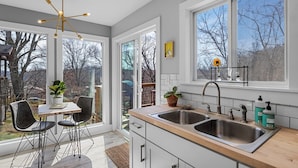 A modern kitchen with a large window, a dining area with chairs, and a pendant light. - Bright and Tranquil Guesthouse! (Woodfin)