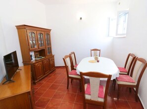 A dining area with a round table, six chairs, a wooden cabinet, and a television on a stand. - Three Bedroom Apartment With Terrace (Pag)
