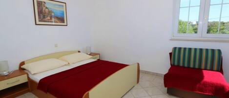 Camera da letto con un letto, comodino, lampada e finestra con vista sul verde.