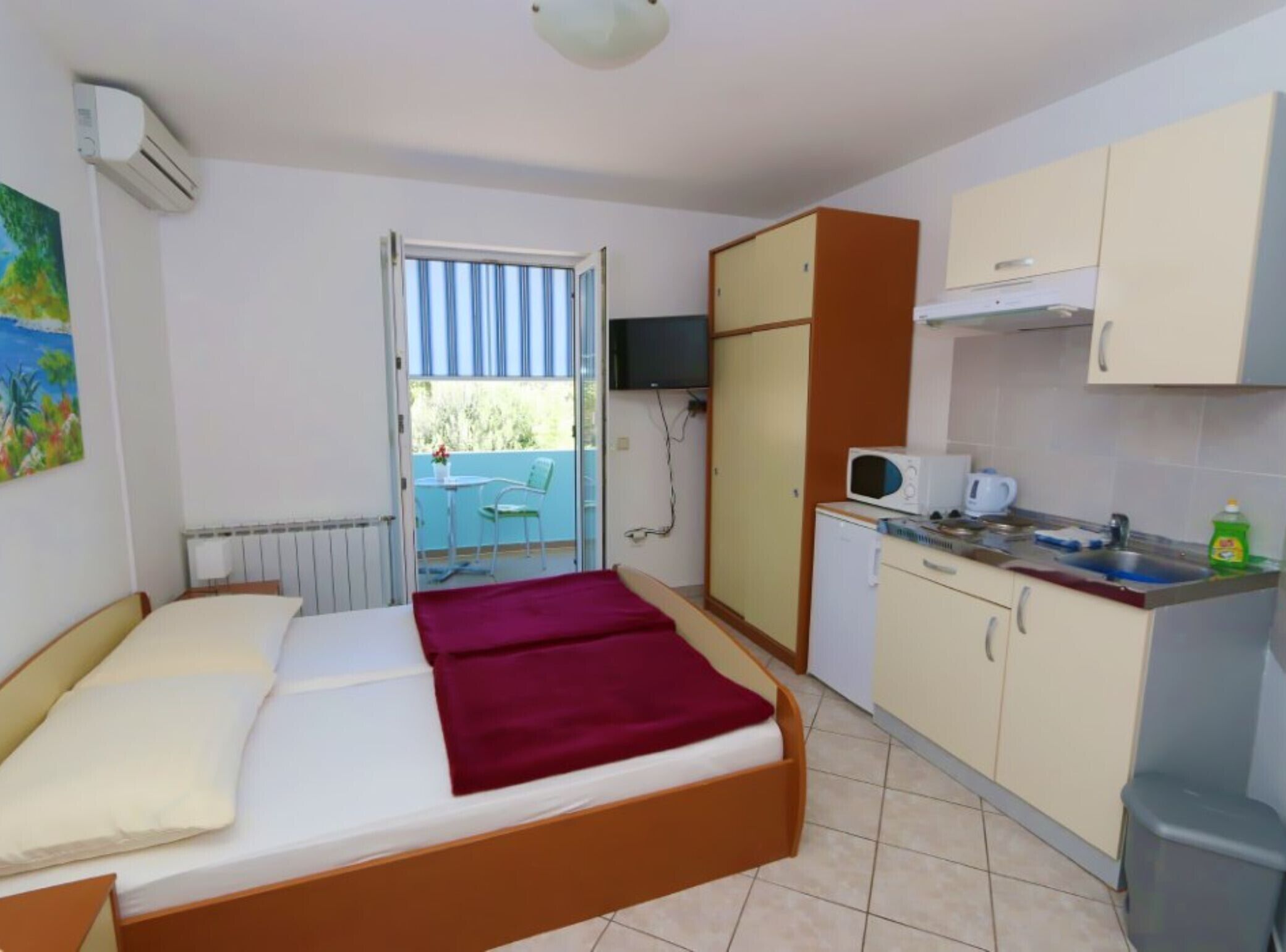 Quarto compacto com cama, cozinha compacta, mesa pequena e varanda com vista.