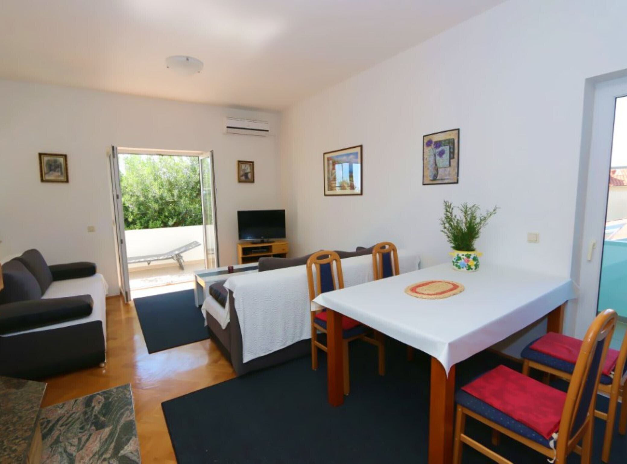Une chambre avec un lit, une télévision, une table à manger avec des chaises et un balcon avec un fauteuil.
