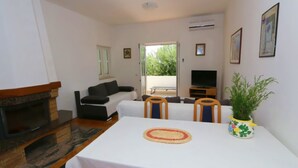 Uma sala de estar com lareira, um sofá, uma televisão e uma mesa de jantar com cadeiras.