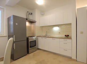 A kitchen with white cabinets, a stainless steel refrigerator, a stove, and a sink.