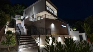 Een moderne villa met twee verdiepingen, een balkon, een trap en een goed verlichte entree.