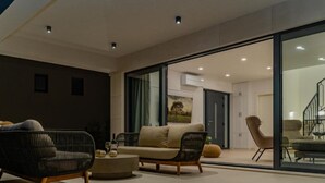 Een moderne woonkamer met een bank, stoelen en een salontafel. Er is een glazen deur naar een eethoek.