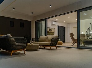 Ein modernes Wohnzimmer mit einer Couch, Sesseln und einem Couchtisch. Eine Glastür führt zu einem Essbereich.