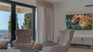 Een moderne woonkamer met een grote televisie, comfortabele zitplaatsen en uitzicht op de omgeving.