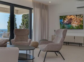 Ein modernes Wohnzimmer mit großem Fernseher, bequemen Sitzmöglichkeiten und Blick ins Freie.
