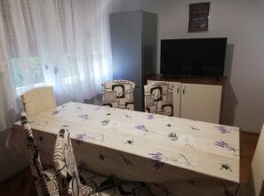 Ein Essbereich mit Tisch, Stühlen, einem Kühlschrank und einem Fernseher.