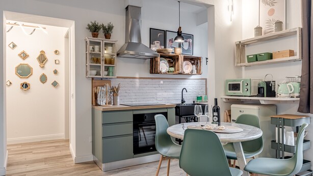 Uma cozinha moderna com forno embutido, área de refeições com cadeiras verdes e painel de azulejos branco.