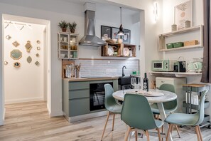 Eine moderne Küche mit Backofen, ein Essbereich mit grünen Stühlen und einer weißen, gefliesten Rückwand.