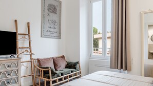 Quarto com cama, penteadeira, televisão, janela com cortinas e quadro pendurado na parede.