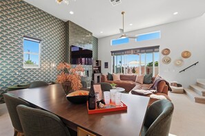 A modern living room with a dining area, large windows, and a patterned wall. - Casa Volare- Pool+Spa, Gated 4BR 3BA 2,400sqft Brand New Desert Retreat (Bermuda Dunes)