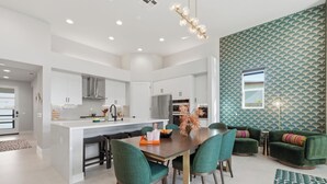 Una cocina moderna con armarios blancos, una isla central y un comedor con sillas verdes.