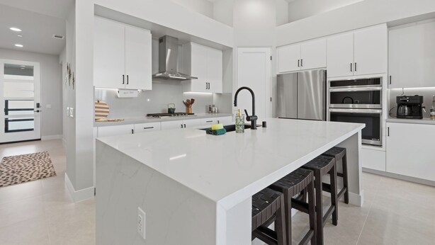 Una cocina moderna con armarios blancos, una isla grande, electrodomésticos de acero inoxidable y un diseño minimalista.
