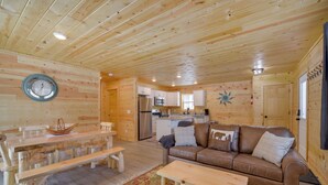 A wooden cabin interior with a dining table, benches, a sofa, a coffee table, and a kitchen area. - Retreat Near Ice Fishing, ATV Trails, Golf, Skiing (Danbury)