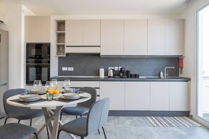 Une cuisine moderne avec des meubles blancs, un plan de travail noir et un coin repas avec une table dressée pour quatre personnes.
