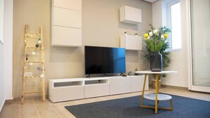 En moderne stue med et fladskærms-tv, hvide skabe, et lille rundt bord og en potteplante.