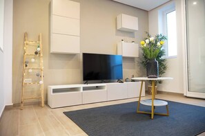 A modern living room with a flat-screen TV, white cabinetry, a small round table, and a potted plant. - `Gibi` Apartment by ELDI (L-Imsida)