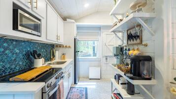 A modern kitchen with white cabinetry, a blue tiled backsplash, and a coffee machine on a shelf.