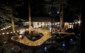A modern outdoor patio with seating and a fire pit, surrounded by trees and string lights. - Wellness Lodge - Sauna, cold plunge, jacuzzi (Morganton)