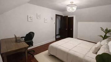 A bedroom with a bed, a desk with a laptop, a chair, a chandelier, and a door.