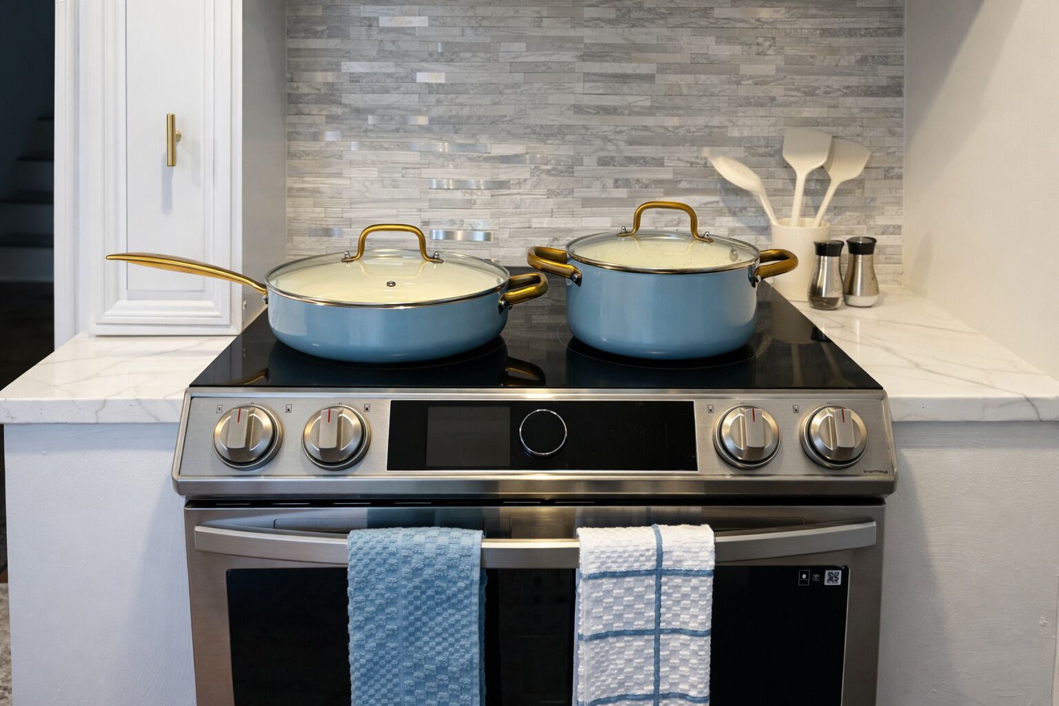 A kitchen with two blue pots on a stove, a white door, and a tiled backsplash.