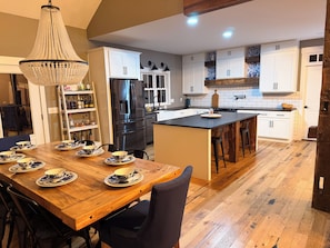 A modern kitchen with white cabinets, a large island, and a dining table set with blue and white plates. - Luxury Waterfront Nolin River Lake House,3BR+Loft,Dock,Lake Toys,Fireplace (Cub Run)