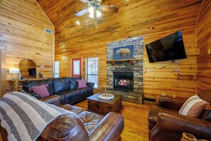 A cozy log cabin interior with a stone fireplace, leather furniture, and a mounted television. - Kodiak Bear-hot tub-playground-location! (Broken Bow)