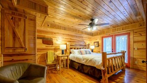 Ein Schlafzimmer einer Holzhütte mit einem Bett, einem Sessel, einem Nachttisch und einem Deckenventilator.