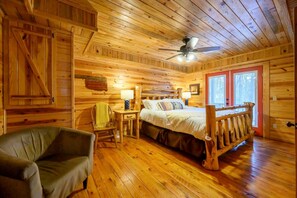 A wooden cabin bedroom with a bed, a chair, a nightstand, and a ceiling fan. - Kodiak Bear-hot tub-playground-location! (Broken Bow)