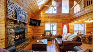 Ein gemütliches Blockhaus-Interieur mit Kamin aus Stein, Ledermöbeln und einem Balkon.