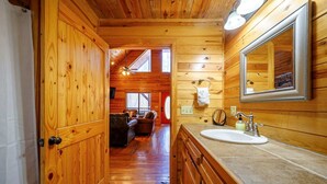 Ein Holzhäuschen im Inneren mit Holztür, einem Badezimmer mit Waschbecken und Spiegel sowie einem Wohnbereich mit Sofa und Kamin.