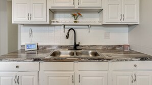 A kitchen with white cabinets, a double sink, a marble countertop, and a small shelf with flowers. - 6 Mi to Downtown Columbus: Quiet Home w/ Yard (Columbus)