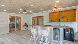 Une cuisine avec un plafond en bois, un coin bar avec deux tabourets de bar blancs et un réfrigérateur.