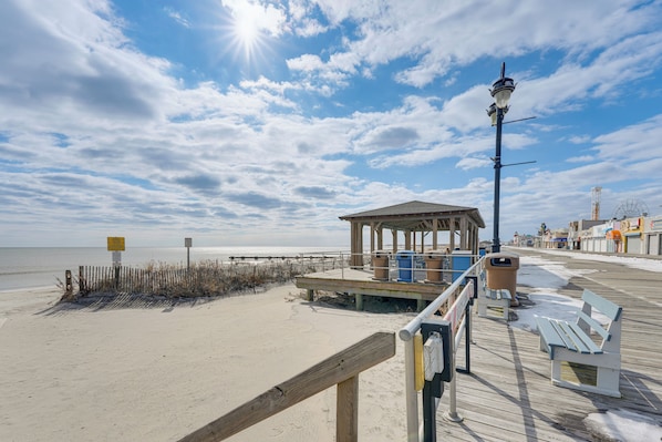 A beach boardwalk with a wooden structure, benches, trash bins, and a lamp post.
