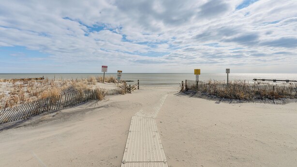A sandy beach with a paved walkway leading to the water, surrounded by dunes and signs. - Walk to Shore! Family Haven w/ Pool in Ocean City (Ocean City)