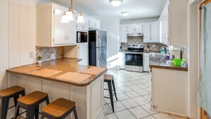 A kitchen with white cabinets, a granite countertop, and a stainless steel refrigerator. There are three stools at the island. - Near Medical Centers & Fort Jackson! Quiet Home (Columbia)