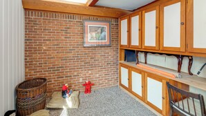 A room with a brick wall, wooden cabinets, a framed picture, a wicker basket, and a red toy. - Near Medical Centers & Fort Jackson! Quiet Home (Columbia)