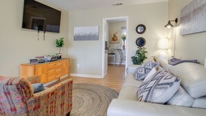Una sala de estar con un sofá, un televisor, un mueble de madera y un comedor al fondo.