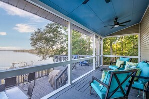 A covered deck with outdoor seating and a view of a lake.