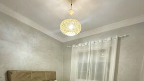 A bedroom with a large bed, a ceiling light fixture, and a window with curtains. - Apartment 4 min Tgv and Beach (Tanger)