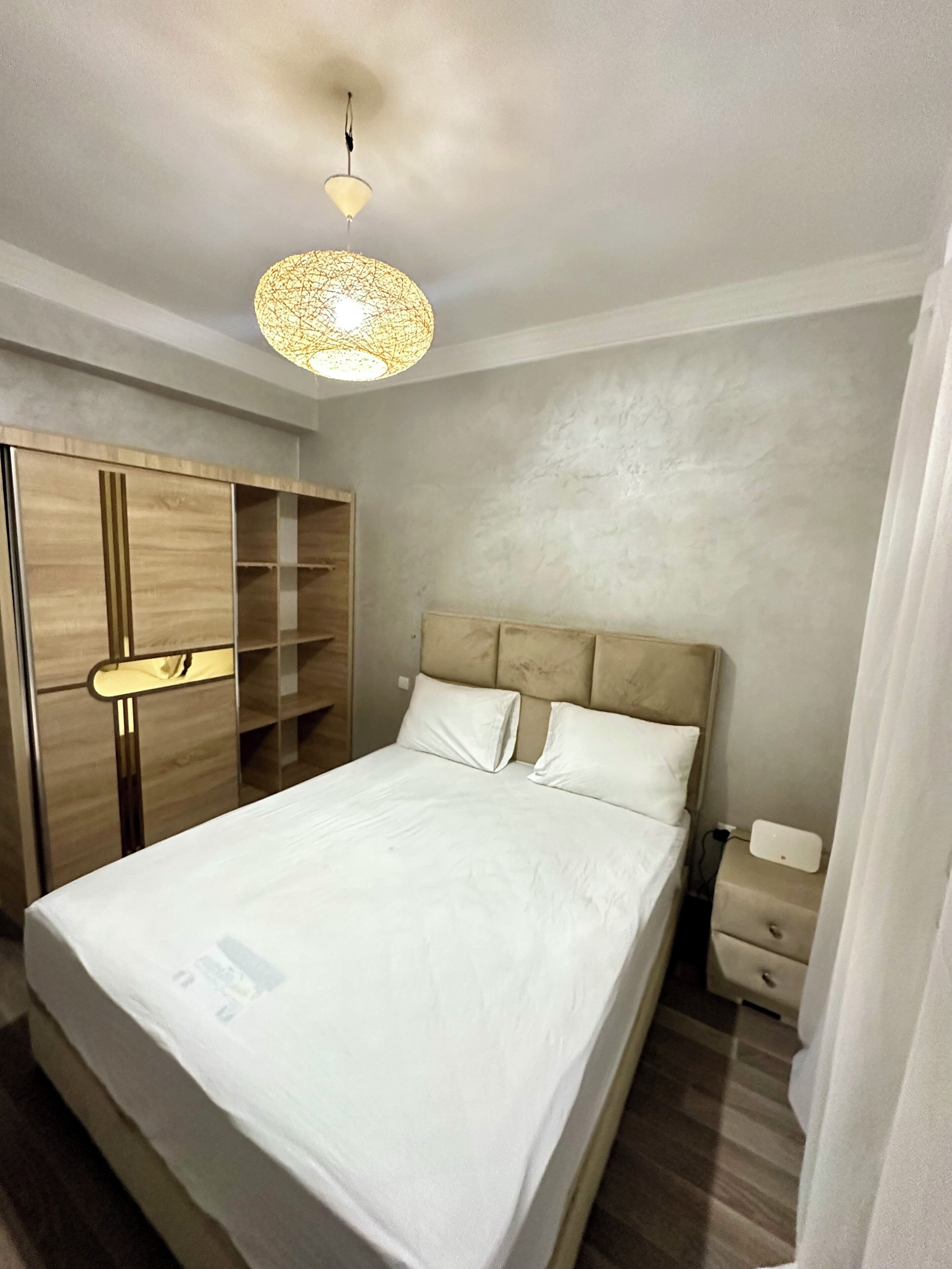 Un dormitorio con cama, armario, mesita de noche y lámpara colgante.