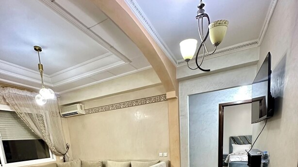 A spacious living room with a sofa, a coffee table, and a TV mounted on the wall. - Apartment 4 min Tgv and Beach (Tanger)