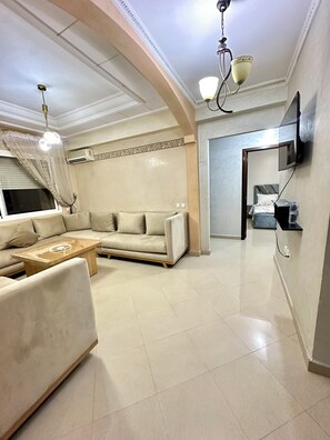 A spacious living room with a sofa, a coffee table, and a TV mounted on the wall. - Apartment 4 min Tgv and Beach (Tanger)
