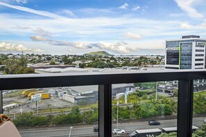 A view from a high-rise building with a clear sky, a parking lot with vehicles, and a commercial building with signage. - Modern High Rise w/ Parking by Zodiak Stays (Auckland)