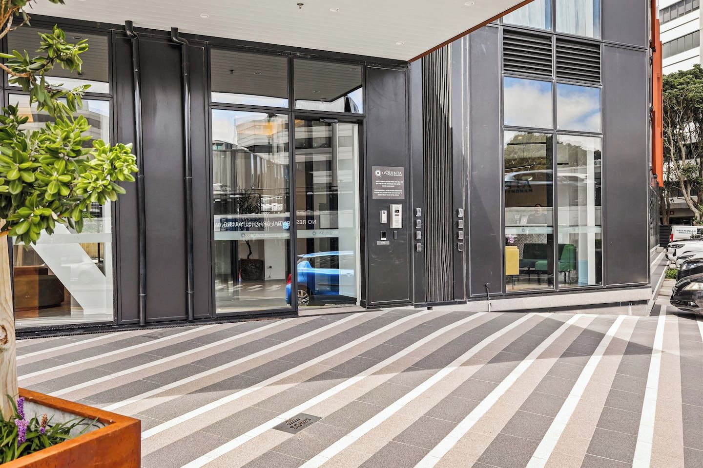 A modern building entrance with glass doors, a car parked inside, and a potted plant outside.