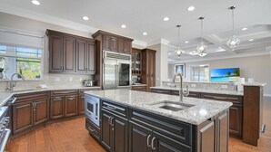 A modern kitchen with dark wood cabinets, stainless steel appliances, and a large island with a sink. - All-in-one Luxury Escape Three Properties, Event Hosting, Private Pond & Full Gym (Jacksonville)